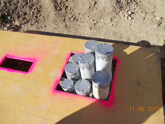 Multiple white PVC pipes bundled together, capped with tape, and placed in a square cutout with pink spray paint marking the edges.