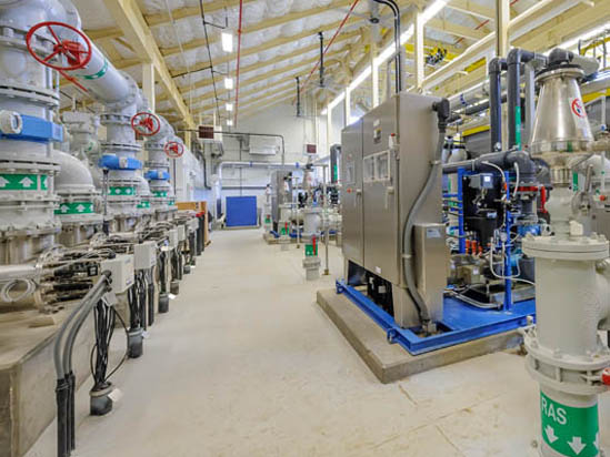An industrial facility with pipes, control panels, and machinery, featuring red valve wheels and labeled equipment.