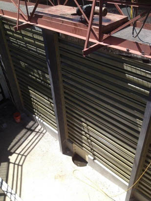 Large slatted industrial structure with metal framework and shadows visible on concrete ground.