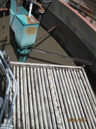 Industrial machinery with metal spiral rods over a water tank, possibly part of a wastewater treatment system.
