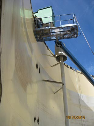 A person on a boom lift working on the side of a large industrial structure.