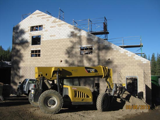A construction site with a yellow telehandler in front of a multi-story building. Scaffolding is visible.