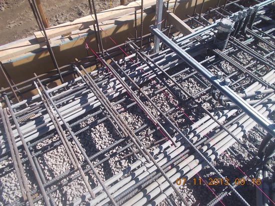Concrete rebar framework with gravel, pipes, and wooden formwork at a construction site. Date: 07/11/2013.