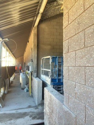 Construction site with brick walls, a blue lift, and two workers in the background.