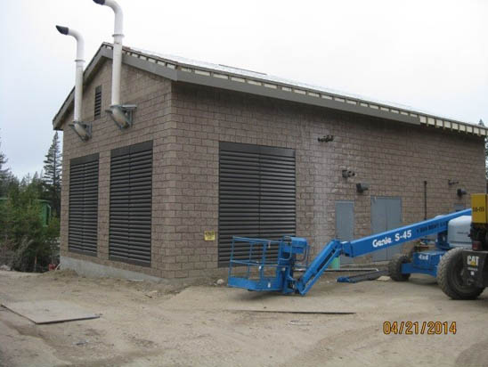 A brick building with two vent pipes, surrounded by construction equipment, including a blue Genie S-45 lift.