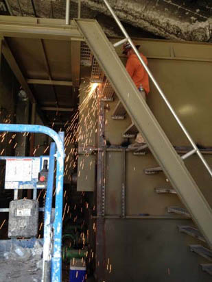 A person welding on a metal structure with sparks flying, in an industrial setting.
