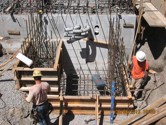 Construction site with two workers, rebar framework, and concrete walls.