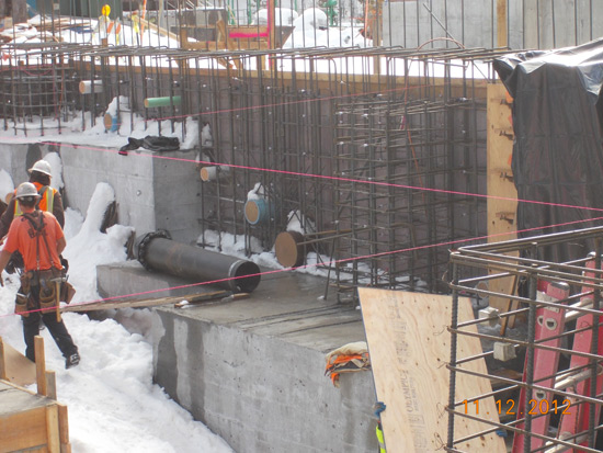 Construction site with workers in snow, steel reinforcements, and concrete structures.