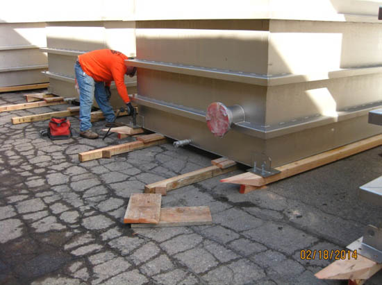 A person is working on large industrial equipment, with wooden planks and tools on a cracked pavement.