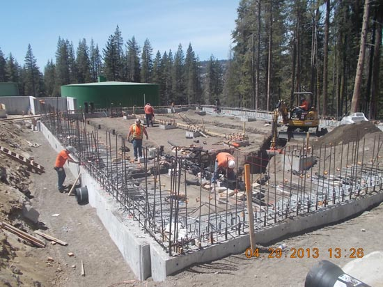 Construction site with workers setting up rebar for concrete. Surrounded by trees and machinery.