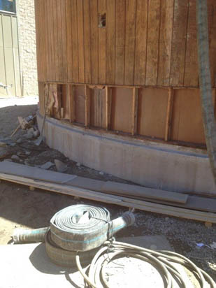 A partially constructed wall with exposed wooden framing and a coiled hose on the ground nearby.