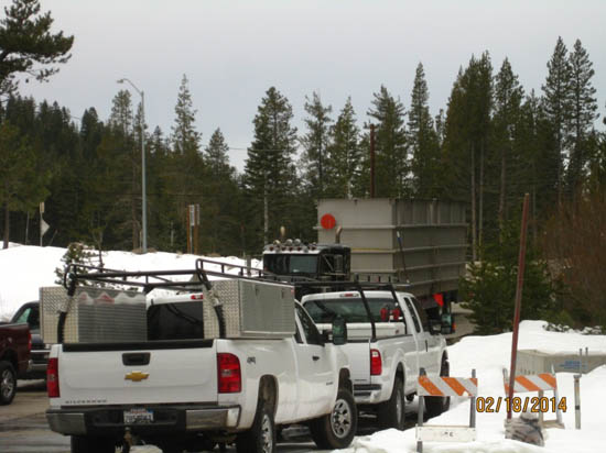 Trucks parked on a snowy road with trees in the background.