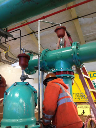 A worker inspects large industrial pipes and valves indoors.