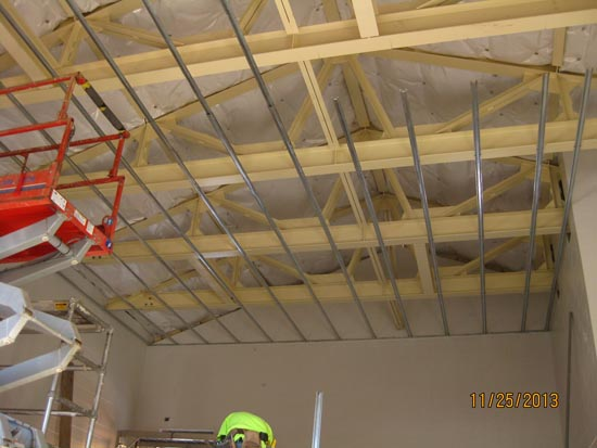Construction site with wooden roof trusses, metal framing, and worker in a safety helmet. Date stamp: 11/25/2013.