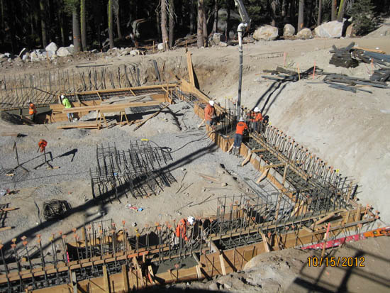 Construction site with workers, building a foundation with rebar and wooden frames in a forested area.