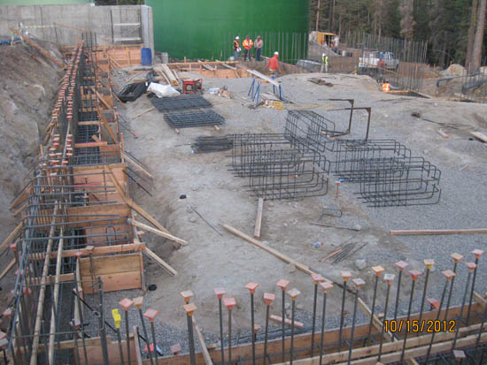 Construction site with rebar, wooden frames, and workers in the background.
