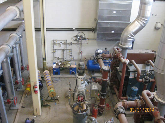 Industrial room with pipes, valves, and machinery, likely for HVAC or plumbing systems.