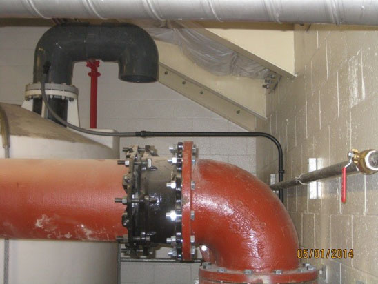 A large red pipe with bolts in an industrial setting, connected to smaller pipes.