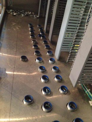 Rows of round metal air vents on a floor, with racks and equipment nearby.