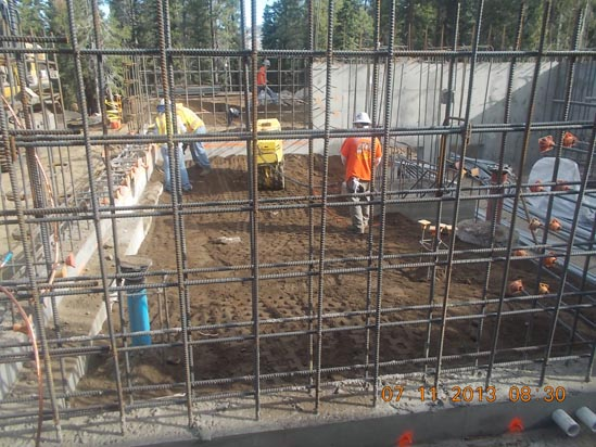 Construction site with workers, rebar structure, and a compacting machine.