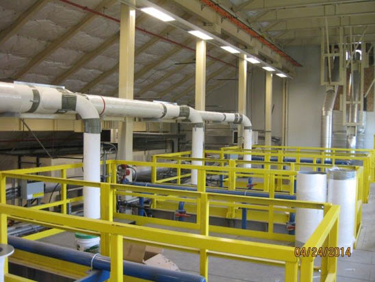 Industrial setting with yellow railings, piping, and machinery under a sloped, insulated roof.