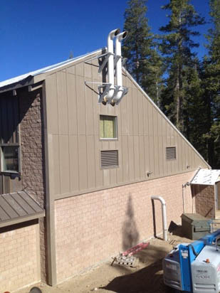 A building with unusual roof pipes, surrounded by trees and construction materials.