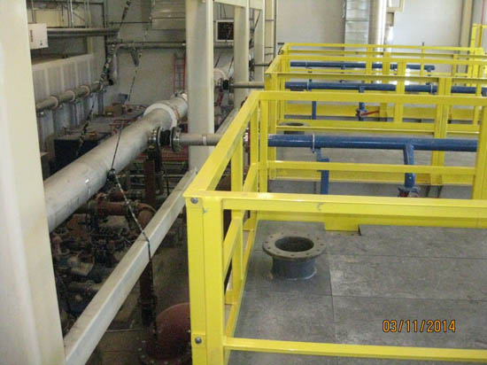 Industrial setting with large pipes, yellow railings, and machinery.