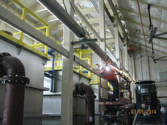 An industrial setting with large pipes and a worker using a tool on a ladder, sparks are visible.