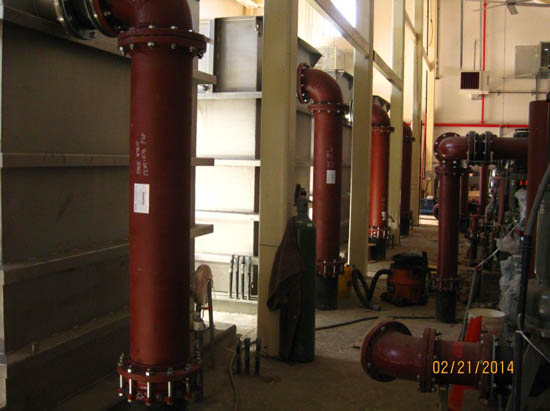 A room with large red industrial pipes, machinery, and a gas cylinder.