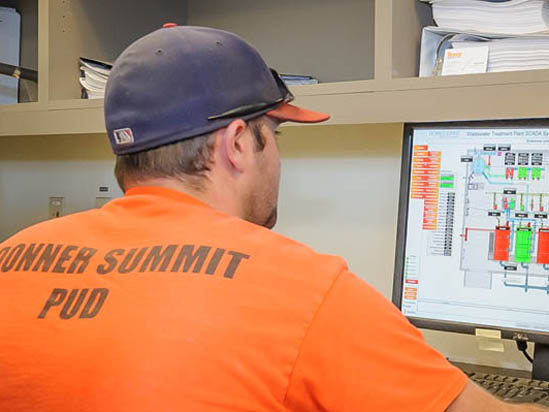 A person in an orange shirt works at a computer displaying technical diagrams.