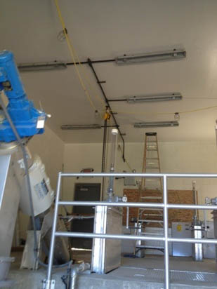Industrial room with machinery, a ladder, metal railings, and ceiling lights.