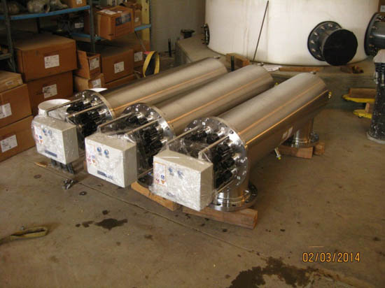 Three large industrial stainless steel cylinders on wooden mounts, surrounded by boxes and equipment in a warehouse.