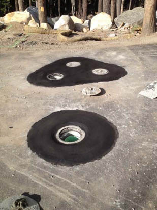 Tire imprints on pavement with circular holes in the center, resembling spaceships. Surrounding trees and rocks are visible.