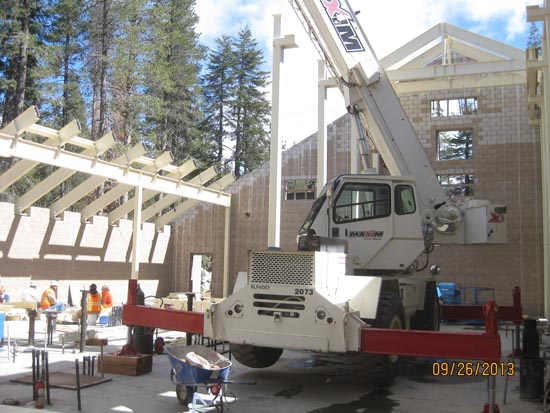 A construction site with a crane, workers, and partially built structures surrounded by trees.