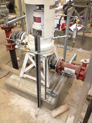 A mechanical setup with pipes, valves, and gauges on a concrete base, likely part of industrial equipment or machinery.