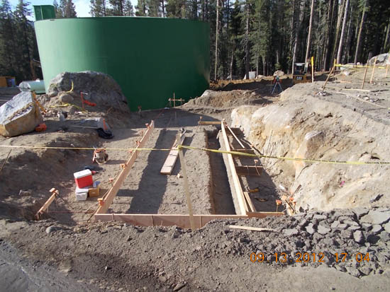 A construction site with a green tank, earth excavation, and wooden frames.