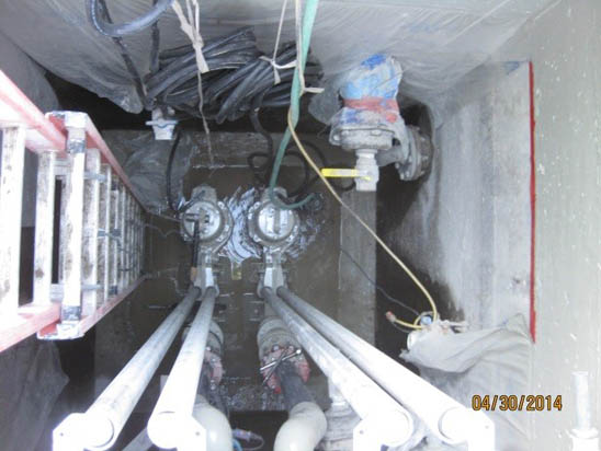 A ladder descends into a utility vault with pipes, valves, and cables visible inside.