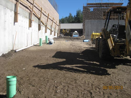 A construction site with building walls, pipes, and machinery on a dirt path.
