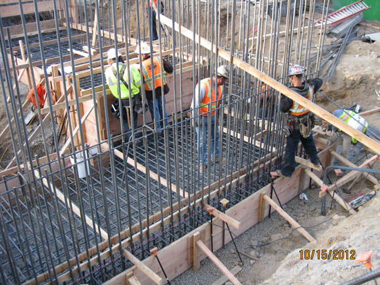 Construction site with workers in hard hats and vests installing rebar for a concrete structure.