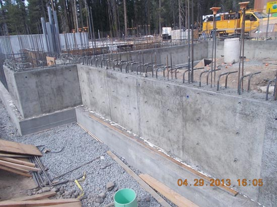 A construction site with concrete walls and rebar, gravel surface, and a yellow truck in the background.