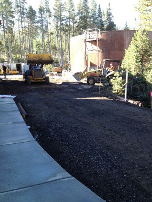 Construction site with heavy machinery and a large cylindrical tank, surrounded by trees.