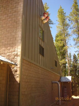 A building with a steep roof, siding, and a life preserver ring above a window, surrounded by tall trees. Date stamp shows May 27, 2014.