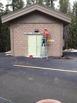 A person on a ladder working on a small utility building labeled "EQ Tank 2 Pump."
