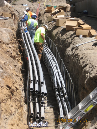 Workers installing electrical conduits in a trench at a construction site.