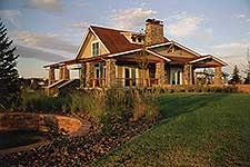 A rustic house with a red roof, chimney, and stone exterior, set in a grassy landscape under a partly cloudy sky.