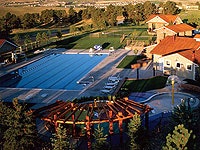 An aerial view of a swimming pool complex with surrounding buildings, trees, and open green space.