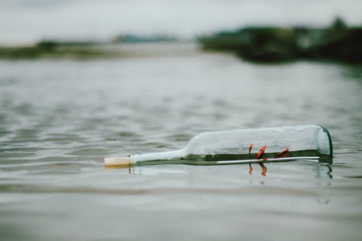 A bottle floating in water with a cork and red ribbon inside.