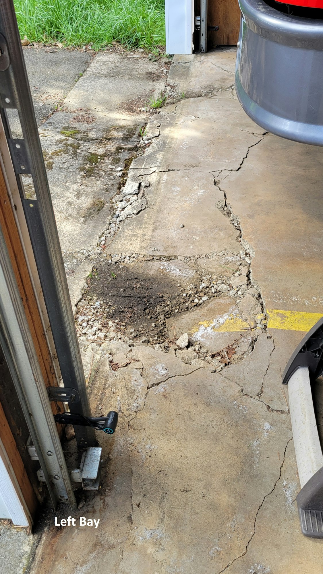 A cracked and damaged garage floor near a door with a partial car bumper visible. Text reads "Left Bay."
