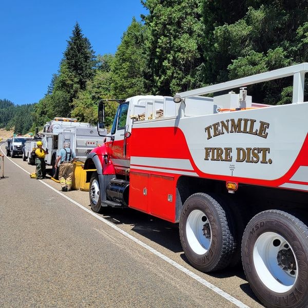 Fire trucks on a road, clear sky, firefighters working, "TENMILE FIRE DIST." on vehicle.