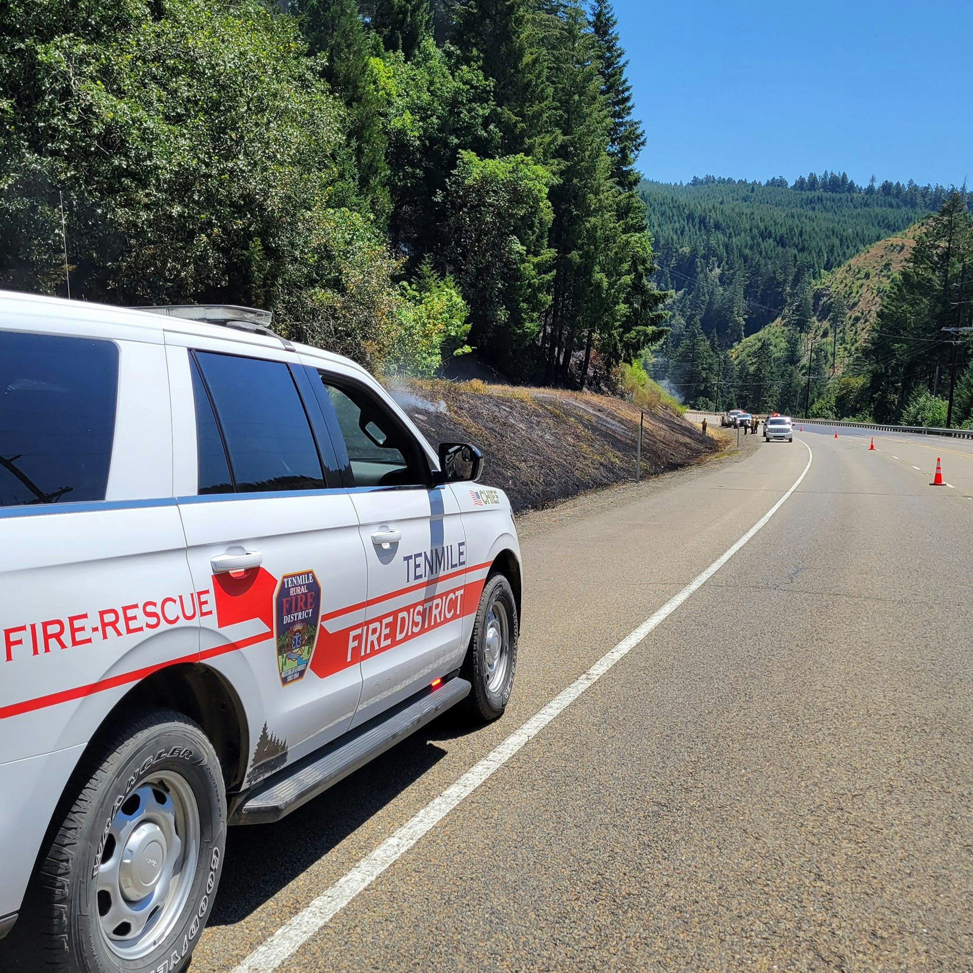 A fire-rescue vehicle parked by a road with burnt grass on the side, hinting at a recent fire incident.